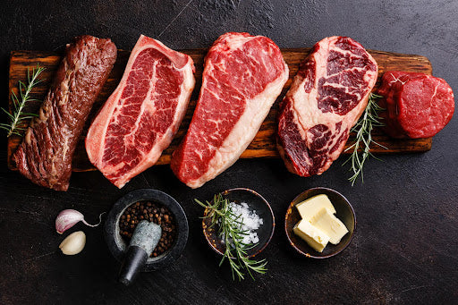 A selection of gourmet meats with sides of black peppercorns, sea salt, garlic, shallot, and butter